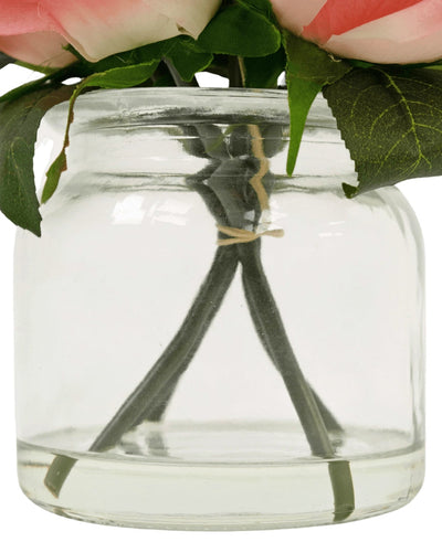 A close-up of the Artificial Rose Bouquet Real Touch Pink 18cm, with green stems tied with twine in a clear glass jar filled with water, topped with pink and green leaves.