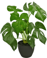 The Artificial Monstera 40 cm in black decorative pot is an artificial Monstera with large, glossy green leaves with natural holes and cracks, in a simple black decorative pot filled with dark soil.