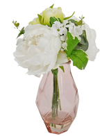 The Artificial bouquet in glass 25 cm has a small bouquet of white flowers with green leaves, arranged in a faceted, light pink glass vase.
