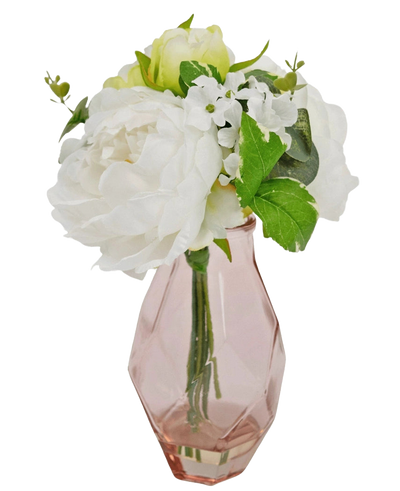 The Artificial bouquet in glass 25 cm has a small bouquet of white flowers with green leaves, arranged in a faceted, light pink glass vase.