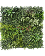 The Artificial Hedge Prestige 100x100 cm UV is a square panel of artificial green foliage with mixed leafy plants, ferns, varied textures and shades of green, plus clusters of small white and red flowers. The background is white.